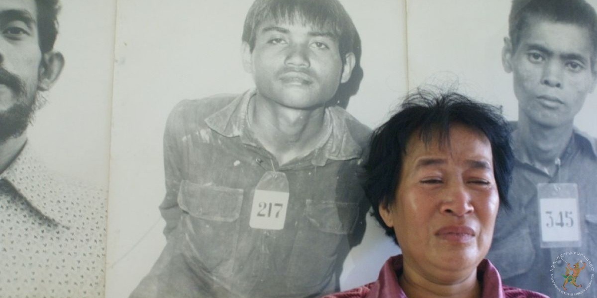 ហ៊ីម មុំ ឈរពីខាងមុខរូបថតប្អូនប្រុសរបស់ខ្លួនឈ្មោះ សាំង គឹមលាង (ពាក់ស្លាក២១៧) ដែលតាំងបង្ហាញនៅសារមន្ទីរឧក្រិដ្ឋកម្មប្រល័យពូជសាសន៍ទួលស្លែងក្នុងឆ្នាំ២០០៨។ ប្រភពរូបថត៖ បណ្ណសារមជ្ឈមណ្ឌលឯកសារកម្ពុជា